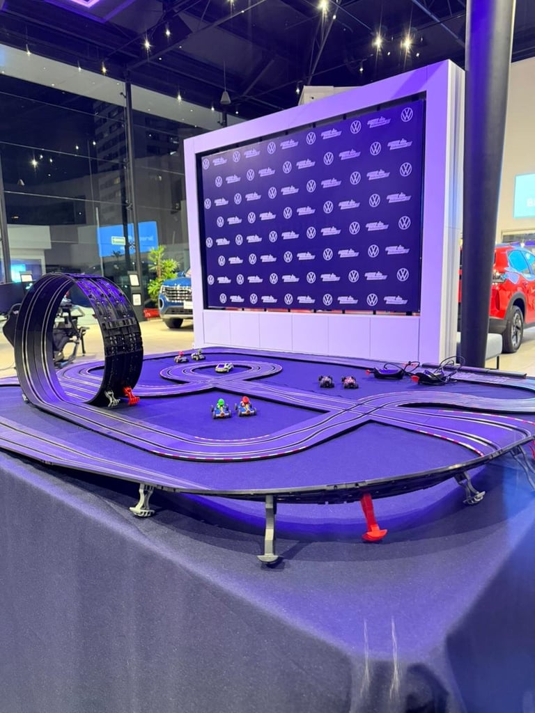 Slot car racing track with purple and blue LED lighting, sponsor backdrop, and miniature vehicles in an indoor automotive exhibition space