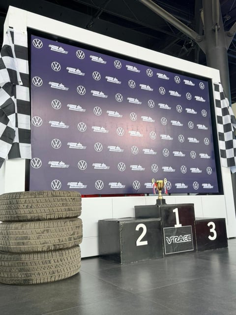 Racing podium with numbered positions 1, 2, 3, Volkswagen branded backdrop, tires and checkered flags on display