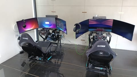 Two gaming setups with racing chairs, multiple monitors, and gaming equipment in a white room